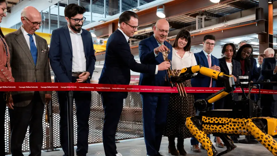 Several people standing near a robotic dog behind a red ribbon during the RIC building opening