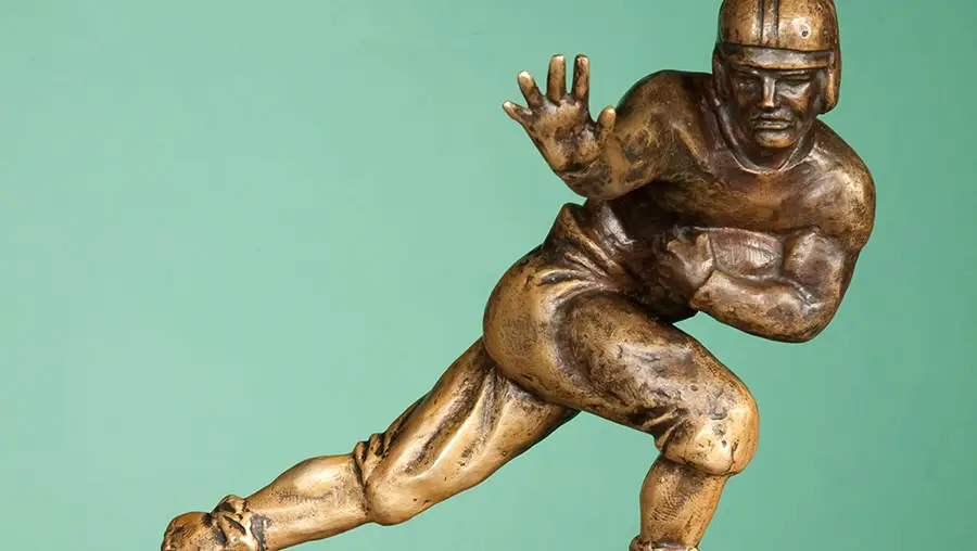 A gold trophy figurine of a football player dressed in 1930s-era uniform and safety gear is set against a teal background.