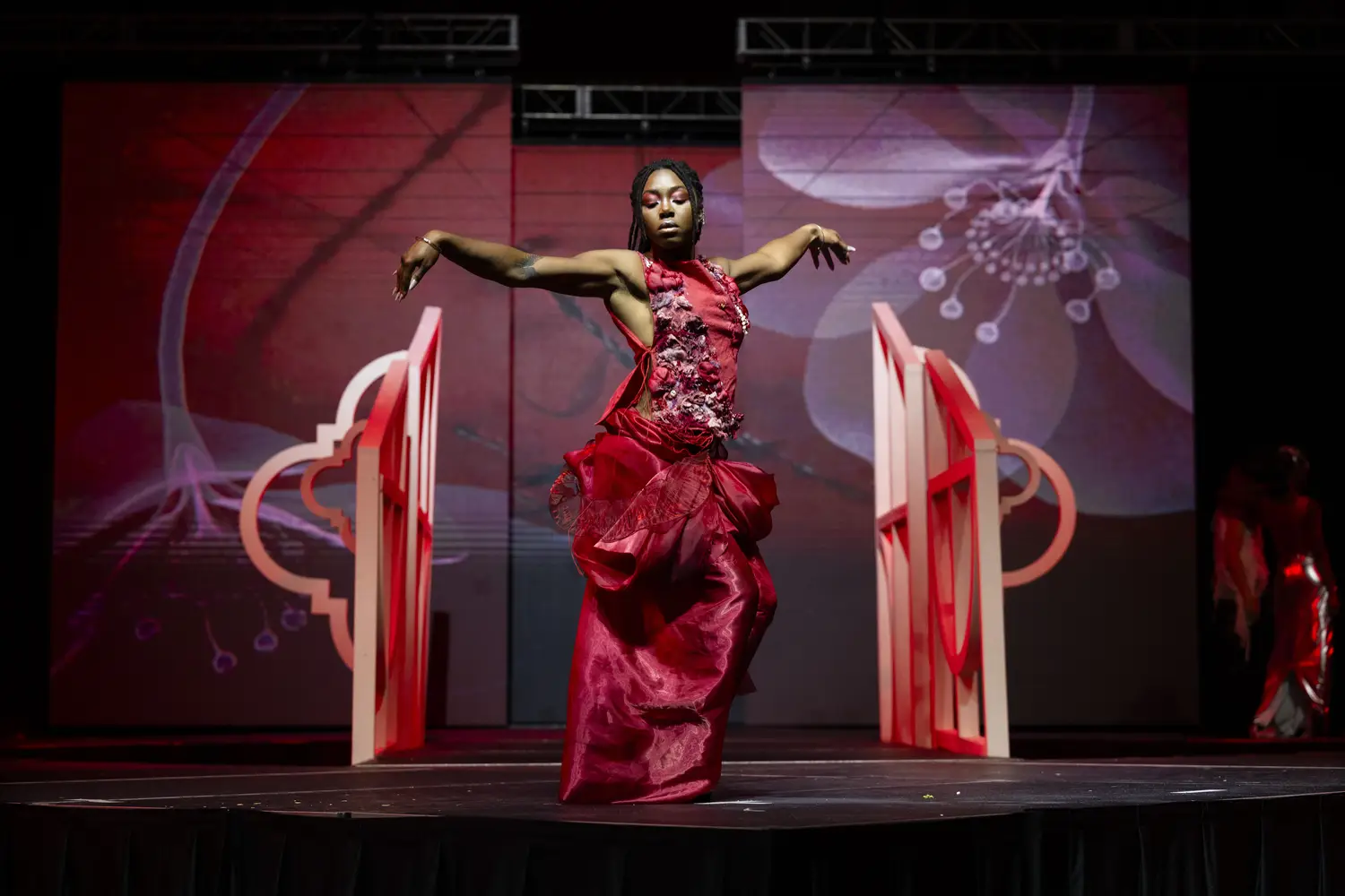 Model wearing a floor-length red dress with large organza swirls in the skirt, and a fitted red top embroidered with red and purple abstract patterns