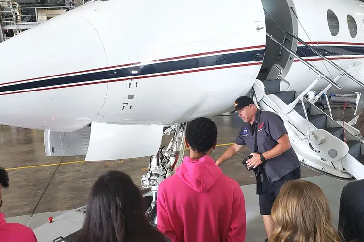 People standing in front of an airplane in a hangar on the ground.
