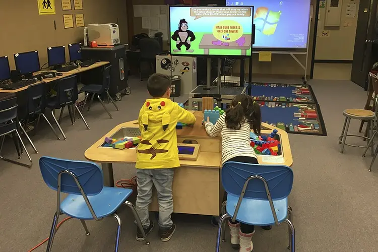 Two children at a table, interacting with objects on the table according to television prompts.