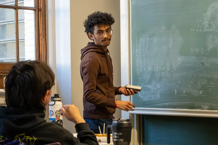 student at chalk board and student seated trying to solve a math problem