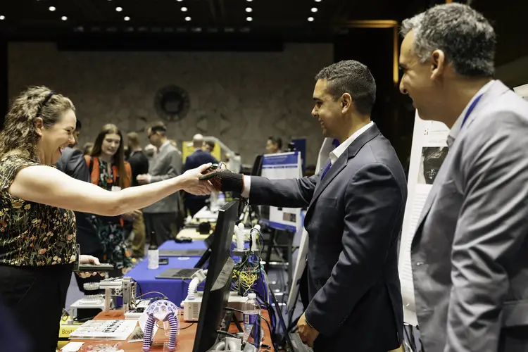 A Congressional staffer shakes the hand of a researcher wearing a special glove that controls a robot