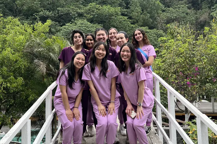 Small group of students wearing scrubs posing outdoors with trees in background