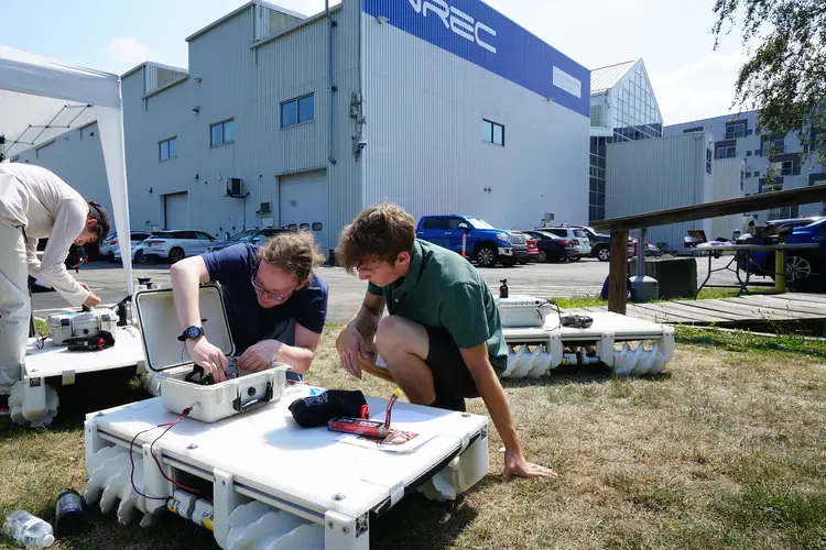 Two students assemble a robot in front of a building labeled NREC