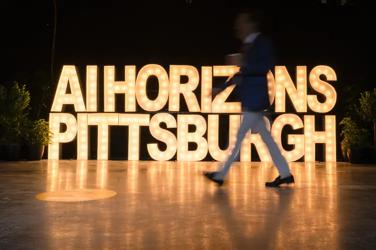 Someone walks by a large sign of the letters "AI Horizons Pittsburgh" spelled out by lightbulbs.