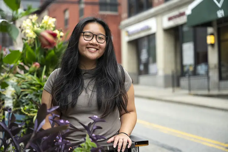 Girl smiling on street near flowers with shops in background