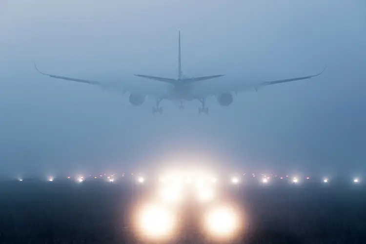 An airplane landing on a runway in heavy fog. The lights along the runway are blurry through the fog.