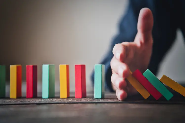 colorful dominos in a line with a hand in the middle to stop some from falling