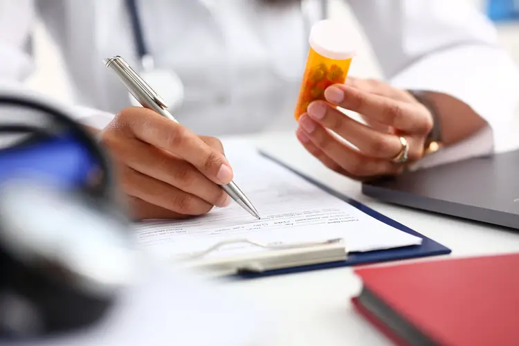 Physician holding a pill bottle, writing a note