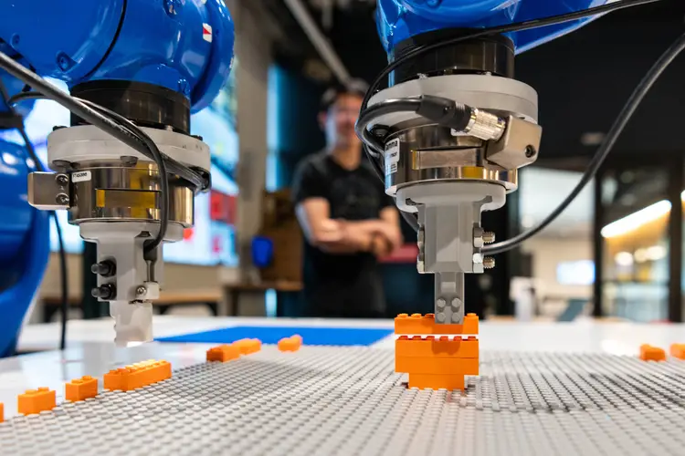 Two blue robotic arms build an orange lego guitar