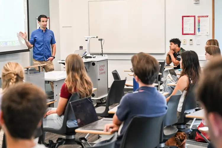 A group of students listen to an instructor at class. 