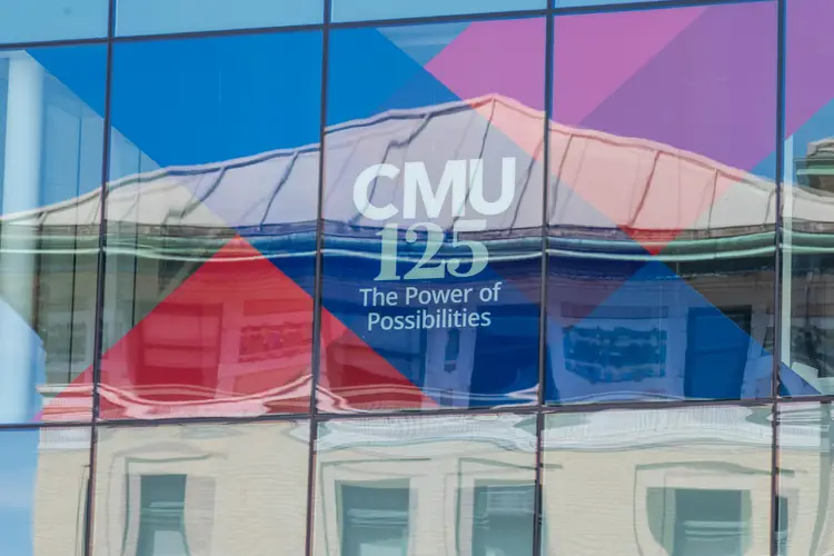 A picture of a window reflecting a building. In the window is a red and blue banner for CMU's 125th celebration. 