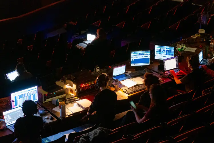 Silhouettes of students sit behind computer screens with their backs to the calendar in a darkened theater.