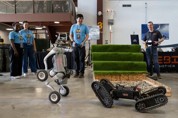 A group of people watch several robots in a demonstration. 
